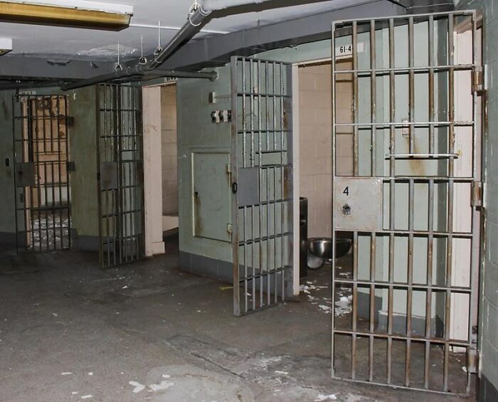 Prison cells with open steel bars in a dimly lit corridor representing crime and imprisonment themes.