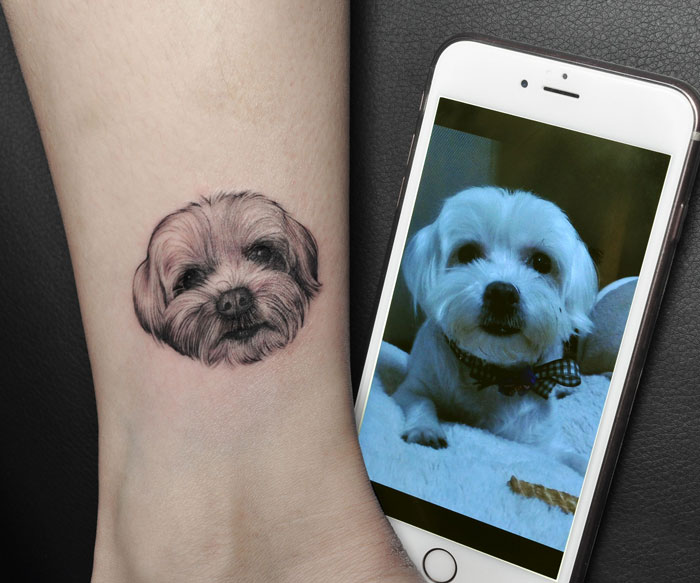Pet tattoo of a small dog on a wrist, beside a similar photo on a smartphone, celebrating furry friends.