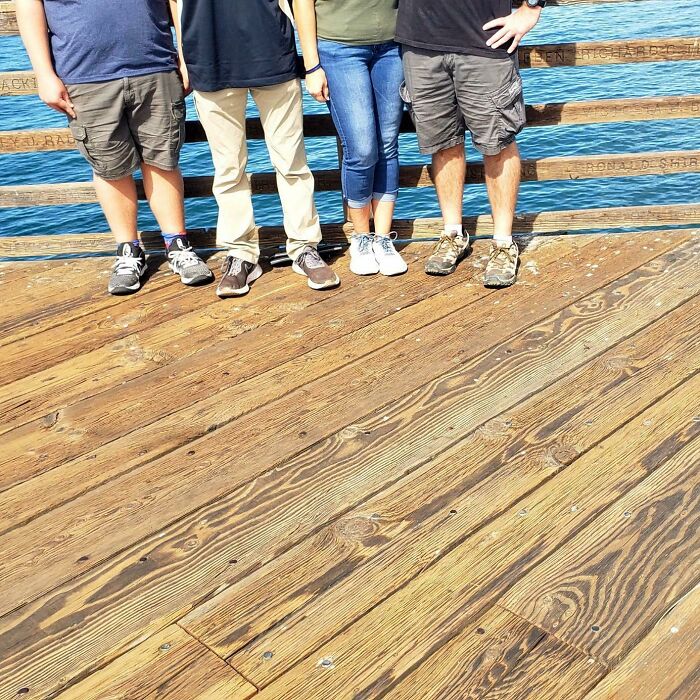 Embarrassing family photo with four people, only legs and feet visible, standing on a wooden pier by the water.