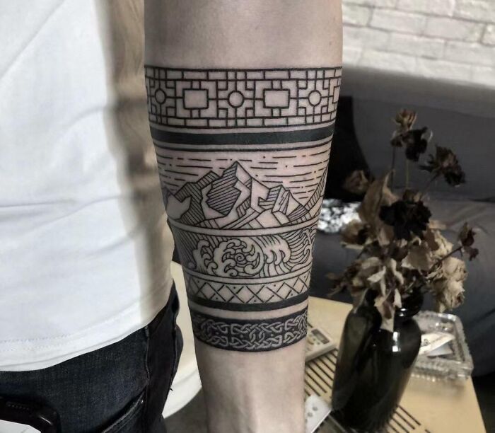 Armband tattoo with geometric patterns and mountain landscape design on forearm.
