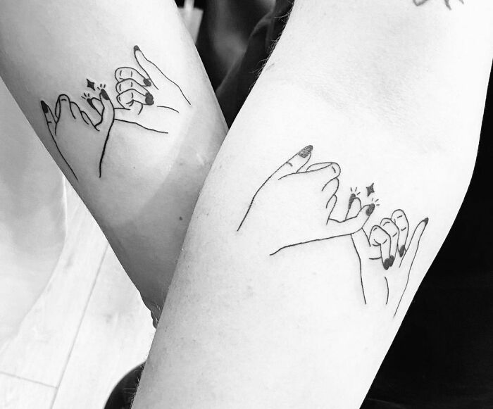 Two arms with matching BFF tattoos of linked pinky fingers, symbolizing friendship and unity.