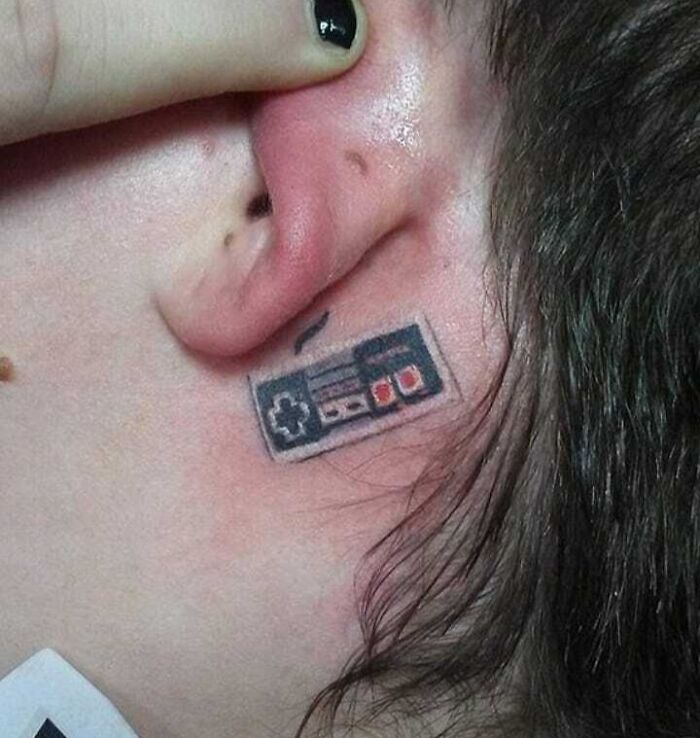 Ear tattoo of a retro game controller, blending subtle and wild design elements.