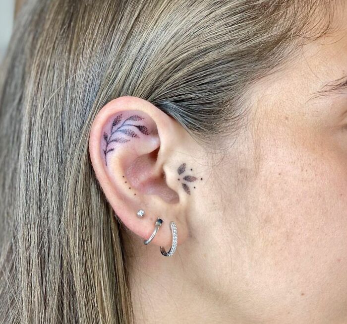 Minimalist floral ear tattoo design with piercings, showcasing subtle tattoo art.