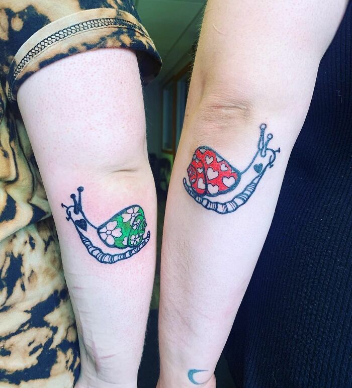 Matching BFF tattoos of snails on arms, one with a green shell, the other with a red shell, symbolizing friendship.