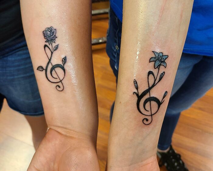 Matching best friend tattoos featuring floral musical notes on wrists.