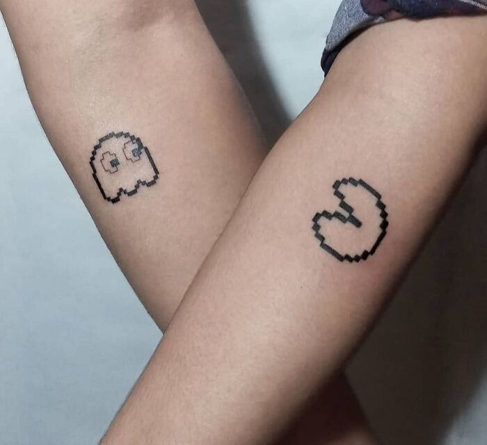 Pixelated best friend tattoos of a ghost and a mouth on two arms symbolizing friendship.