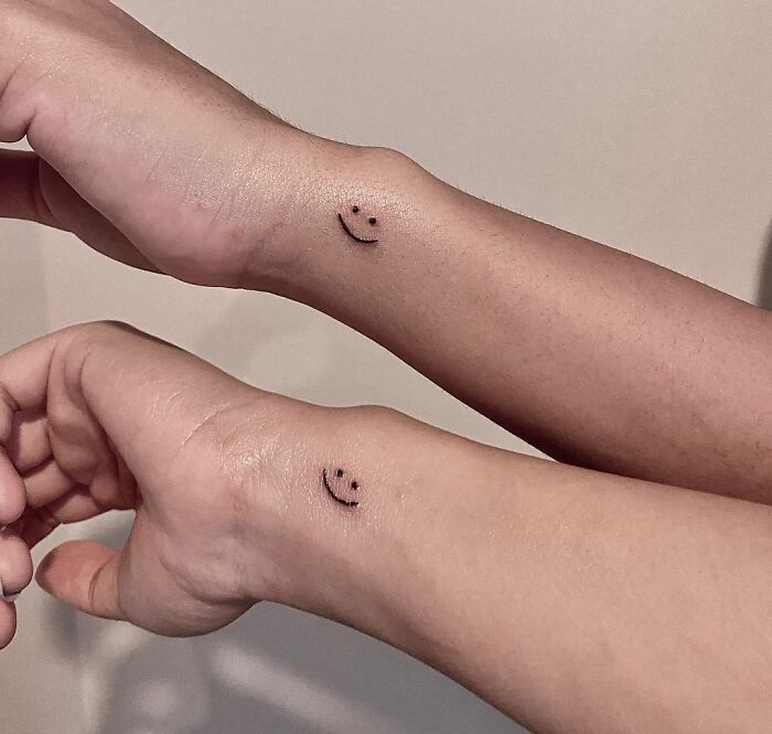 Two wrists with matching smiley face friend tattoos symbolizing friendship.