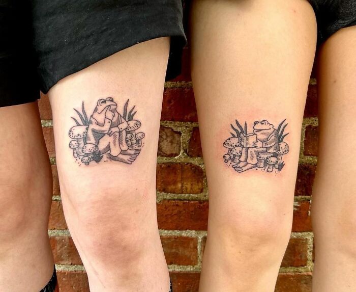 Matching best friend tattoos of sitting frogs, symbolizing friendship, inked on two people's legs against a brick wall background.