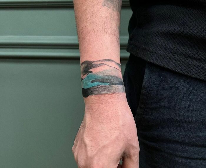 Abstract armband tattoo in black and teal on a man's wrist, showcasing creative tattoo designs and ideas.