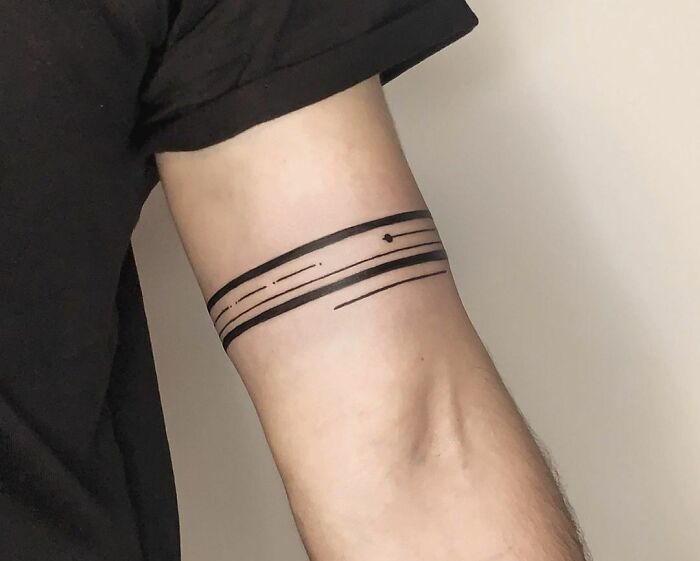 Minimalist armband tattoo design on a person's arm, featuring bold black lines and subtle geometric elements.