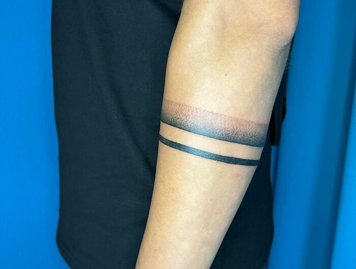 Minimalist armband tattoos on forearm, featuring solid black lines and gradient shading against a blue background.