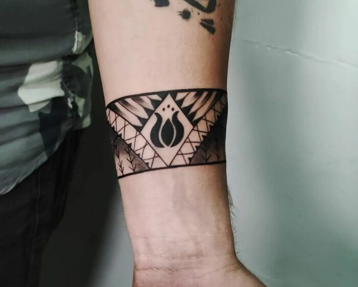Geometric armband tattoo with tribal elements on forearm.