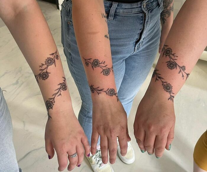 Three people showcasing floral armband tattoos on their forearms, highlighting different tattoo designs.