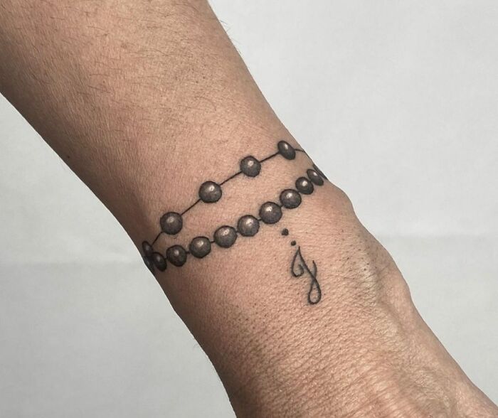 Armband tattoo with dot pattern and small letter design on wrist.
