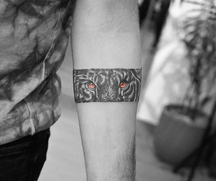 Tiger eyes armband tattoo design on forearm in black and gray, symbolizing strength and courage.