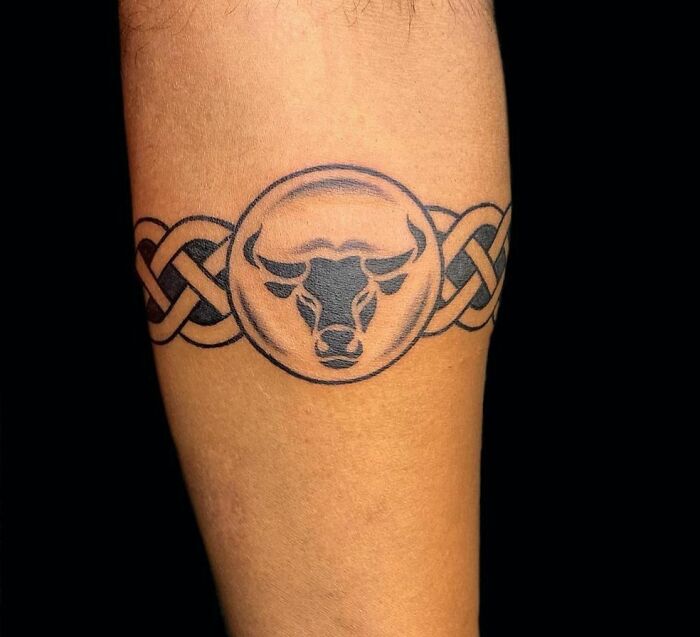 Armband tattoo with intricate bull design in black ink on forearm.