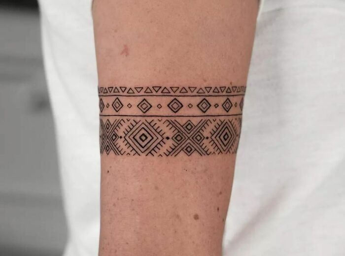 Geometric armband tattoo with tribal patterns on an arm, showcasing intricate design and detailed artistry.