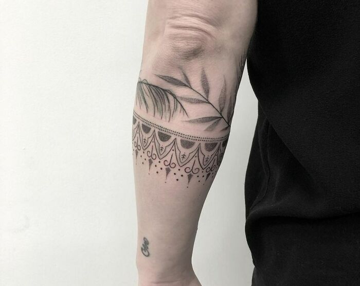Intricate armband tattoo design featuring leaf and ornamental patterns on an arm.