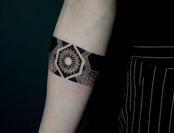 Intricate geometric armband tattoo design with black and gray patterns on a person's arm.