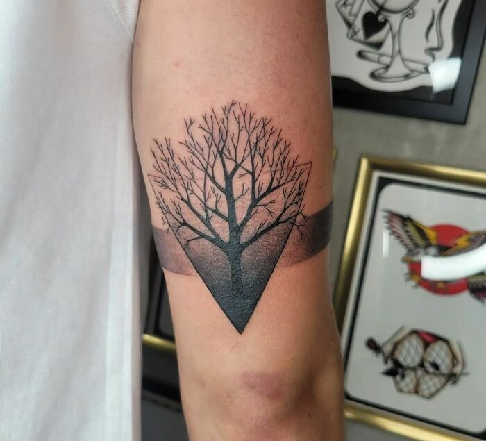 Armband tattoo featuring a detailed tree design on a forearm.