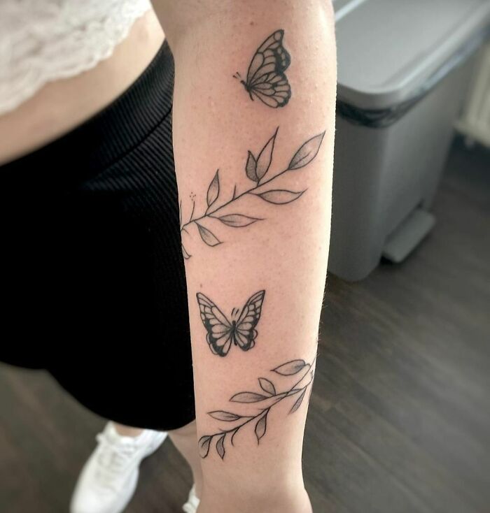 Butterfly and branch design armband tattoo on person's arm.