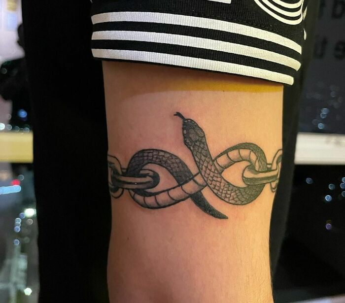 Snake and chain armband tattoo design on a person's arm.