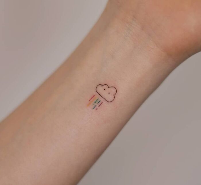 Minimal tattoo of a cloud with colorful rain on an arm.