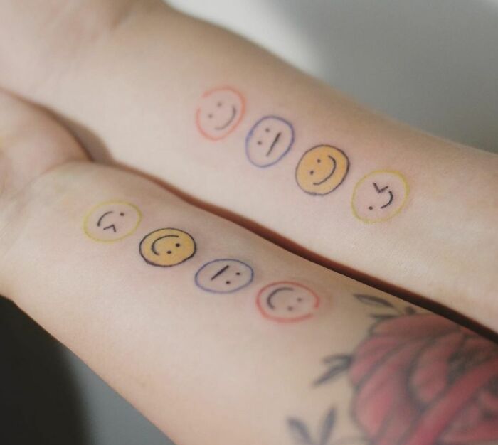 Matching best friend tattoos featuring colorful smiley faces on two forearms.