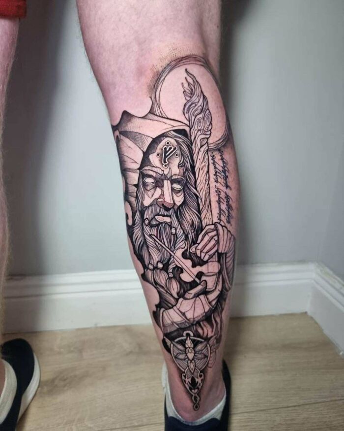 Detailed lower leg tattoo featuring a wizard holding a staff, showcasing intricate line work and shading.