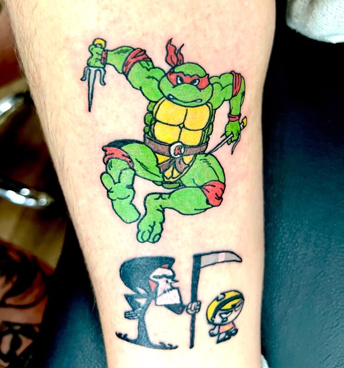 Cartoon tattoo featuring a ninja turtle and comical grim reaper on leg, evoking childhood favorites.