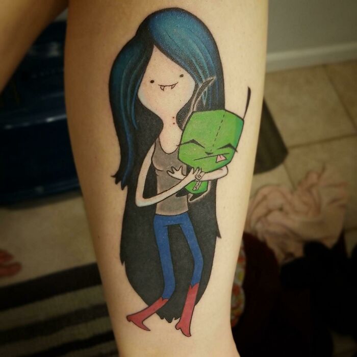 Cartoon tattoo on arm featuring a character with long blue hair and a small green creature.