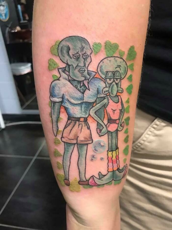 Cartoon tattoo featuring characters from an animated show on an arm, surrounded by green heart shapes.