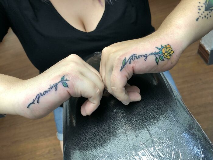 Word tattoos on wrists reading "growing" and "strong" with a yellow rose, highlighting inspirational ink ideas.