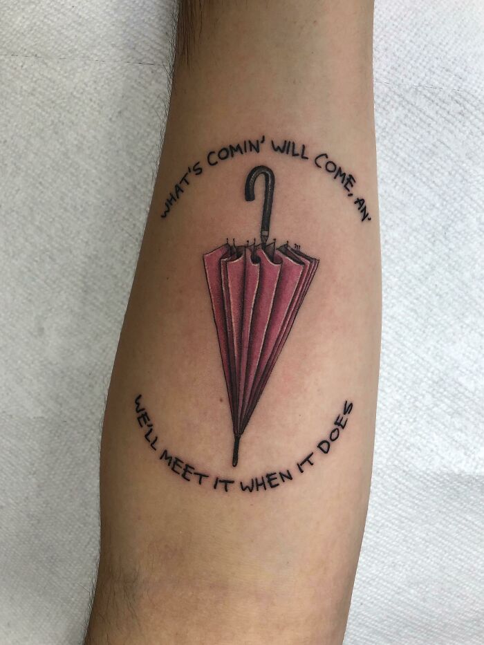Tattoo of a red folded umbrella with inspirational words around it on an arm, perfect for new ink ideas.