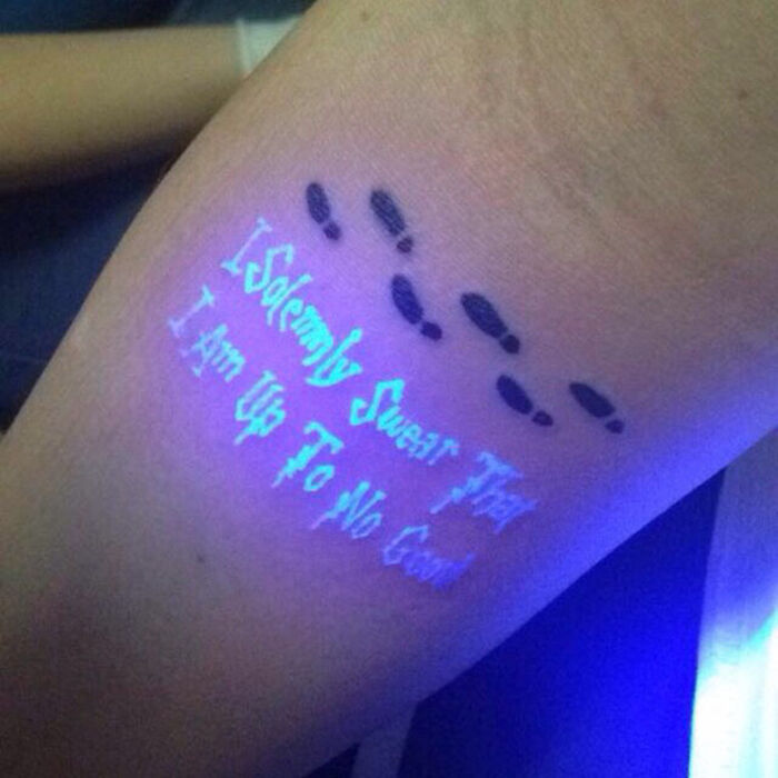UV ink tattoo saying "I Solemnly Swear That I Am Up To No Good" with footprints, a unique word tattoo idea.