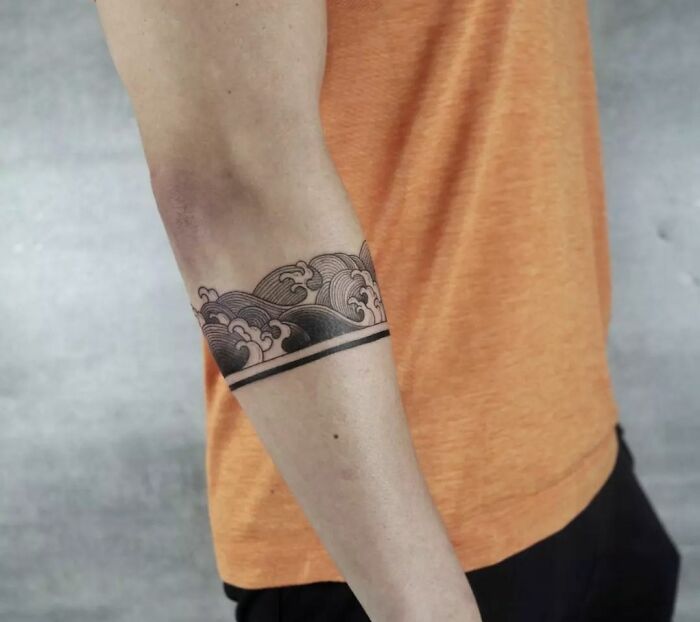 Armband tattoo design featuring ocean waves on a person's arm in an orange shirt.