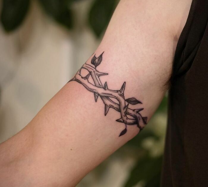 Armband tattoo featuring a vine and thorns design on a person's upper arm.