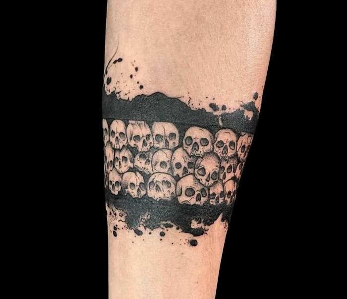 Skull design armband tattoo with black ink details on forearm.