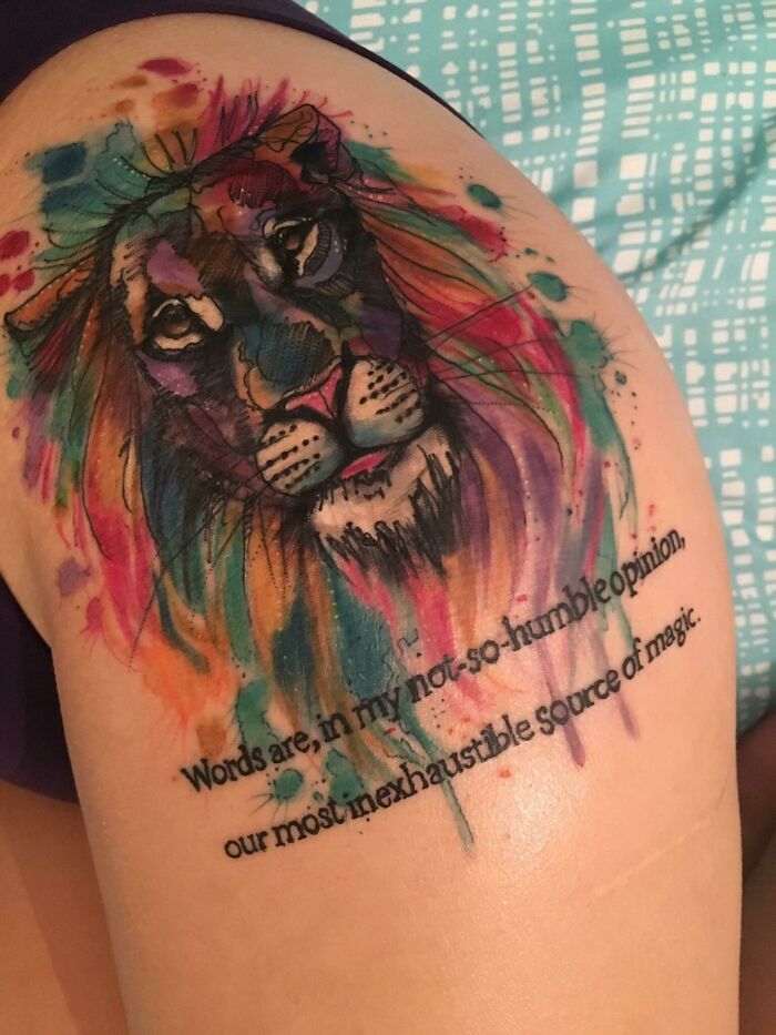 Colorful lion tattoo with quote on arm, showcasing creative word tattoo ideas with vibrant watercolor effect.