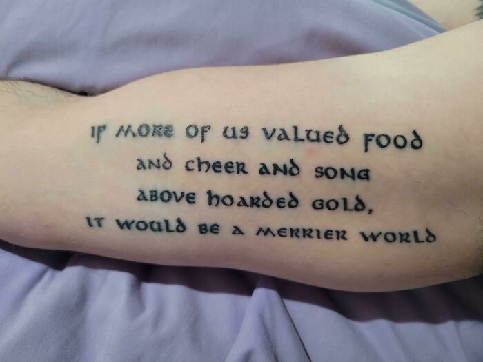 Arm with a meaningful word tattoo about valuing food and cheer over gold, conveying a heartfelt message.