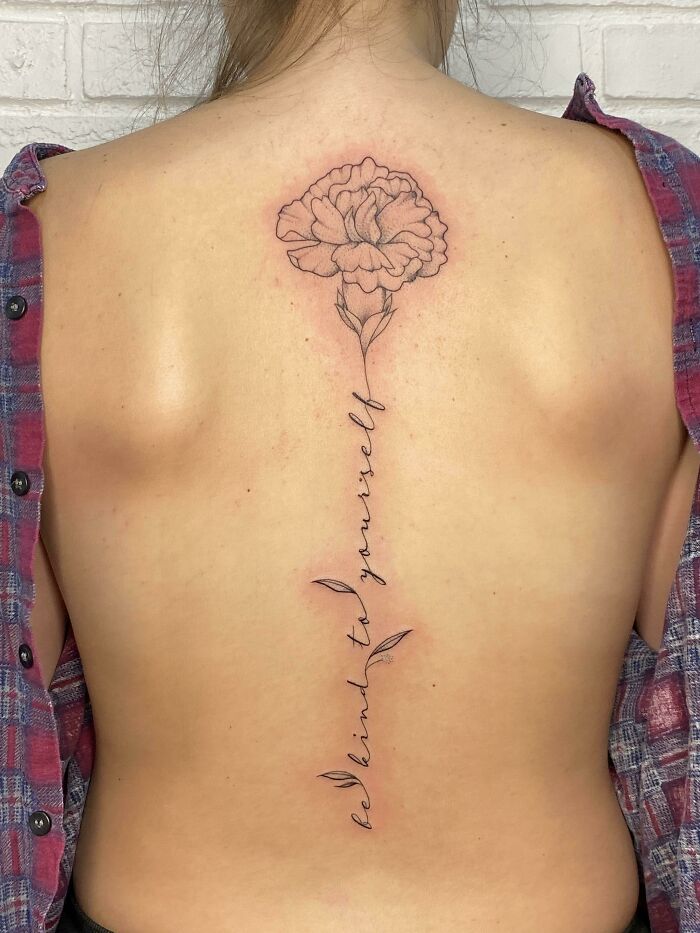 Back tattoo with floral design and words "be kind to yourself," embodying word tattoos theme.