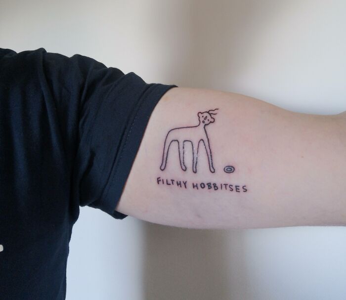 Minimalist line tattoo of a quirky creature with "filthy hobbitses" text on an arm, related to word tattoos.