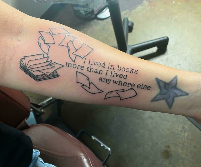 Word tattoo on forearm with book and star design, featuring quote about living in books.