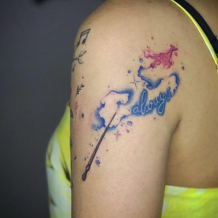 Watercolor tattoo with blue clouds and the word "always," featuring a wand on upper arm.