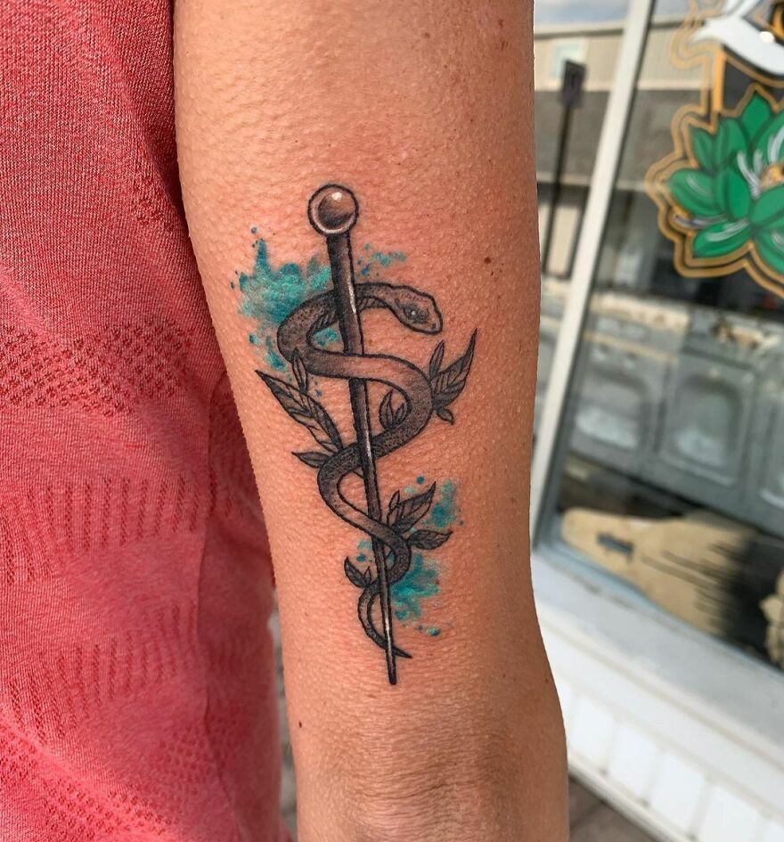 Watercolor tattoo of a staff with a snake and leaves on an arm, featuring turquoise accents.