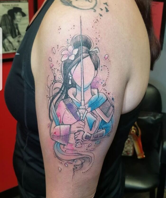 Watercolor tattoo of a warrior woman in vibrant pink and blue ink on an arm.