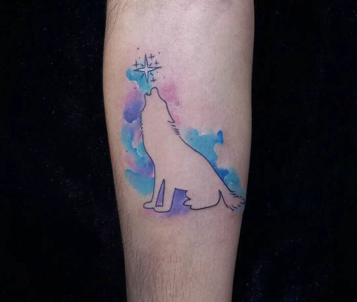 Watercolor tattoo of a wolf howling with stars above, featuring ethereal blue and pink hues.