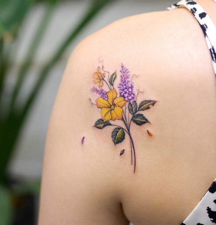 Watercolor tattoo of yellow and purple flowers on a person's shoulder, showcasing an ethereal design.