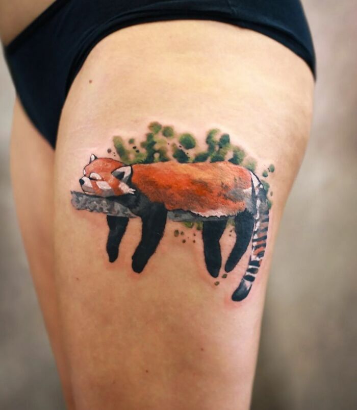 Watercolor tattoo of a red panda with green foliage on the upper thigh, showcasing beautiful tattoo art.