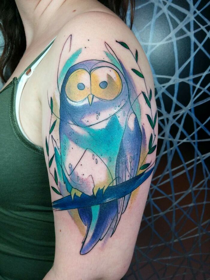 Watercolor tattoo of an abstract owl on an arm, featuring vibrant blues and greens for inkspiration.